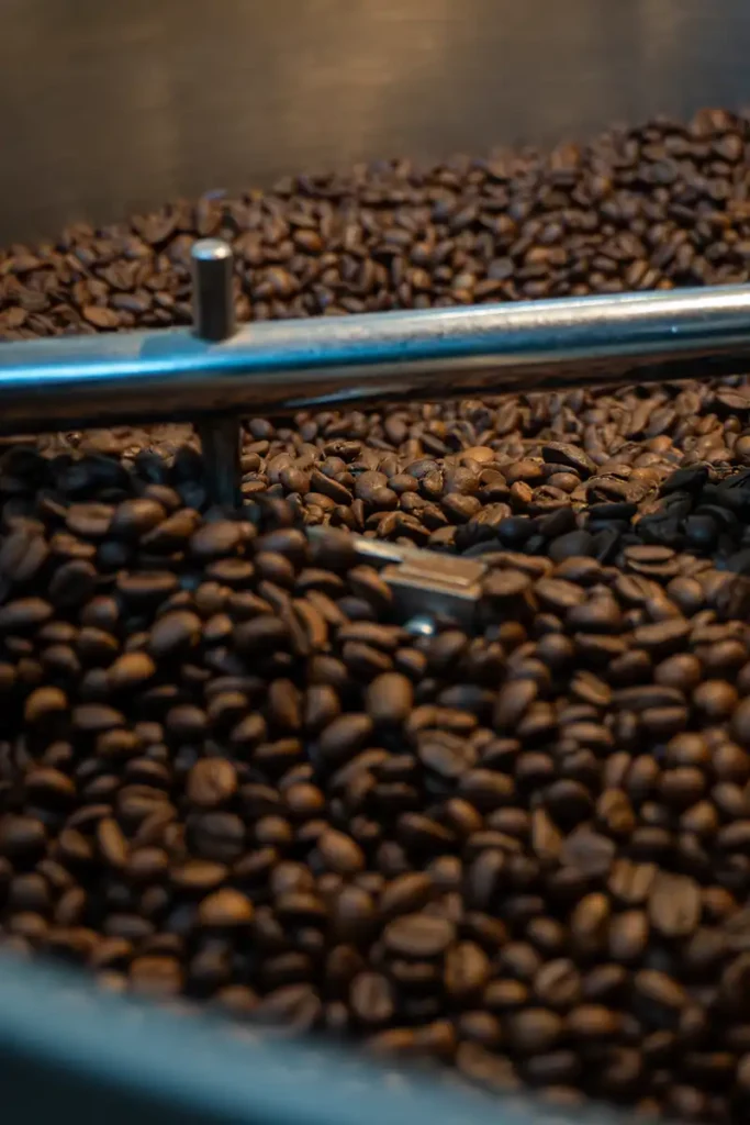 Frisch geröstete Kaffeebohnen in einem Trommelröster mit einem Metallarm im Vordergrund.